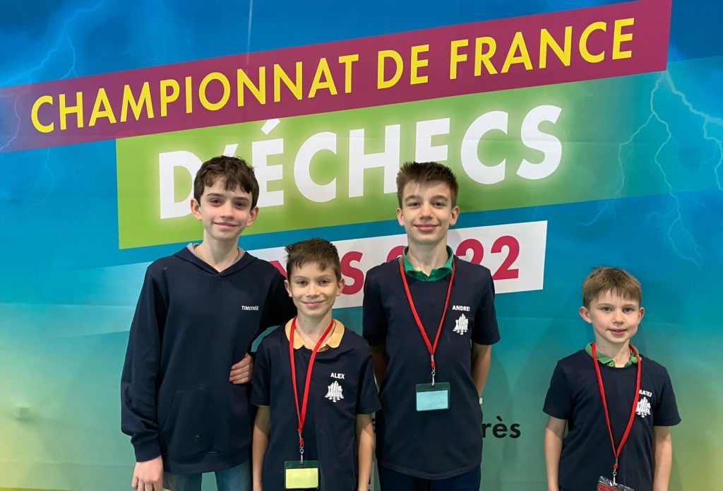 Quatre jeunes joueurs du club posent devant la banderole du Championnat de France d'échecs 2022.