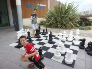 Deux jeunes joueurs posent sur un échiquier géant en plein air devant un centre commercial à Dieppe.