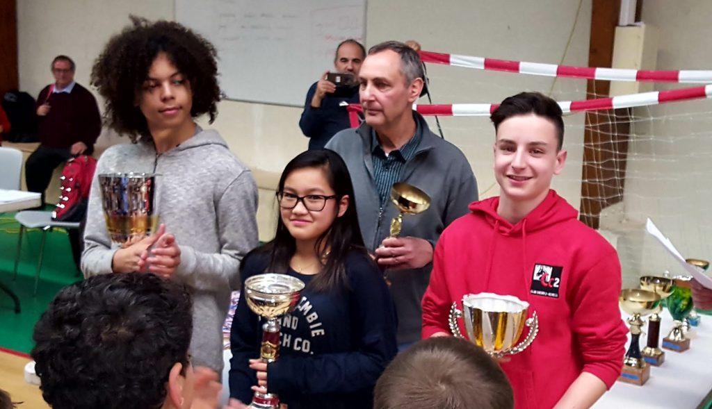 Trois jeunes lauréats brandissent leurs coupes aux côtés d'un organisateur lors de la remise des prix.
