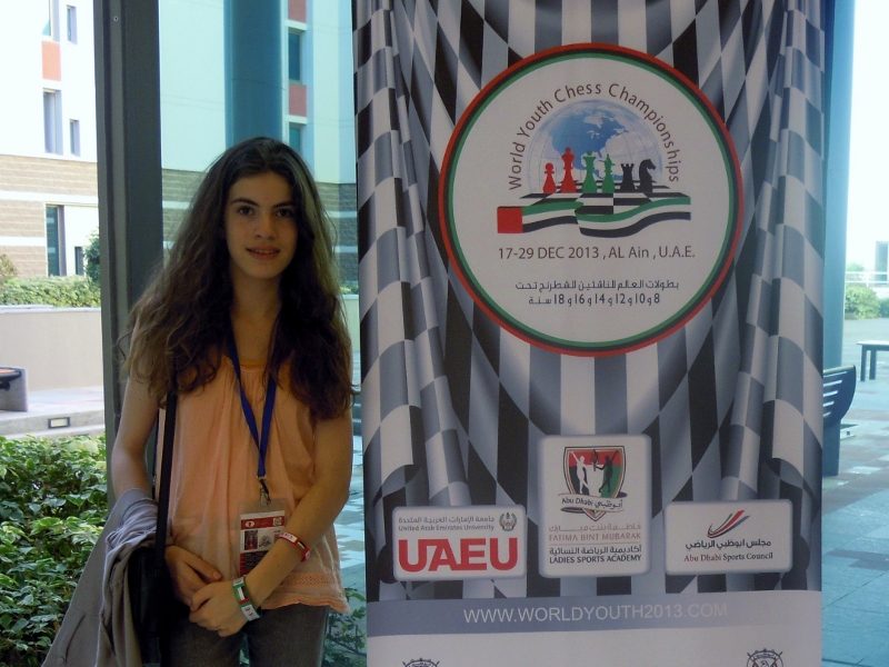 Une jeune joueuse pose devant le kakemono du World Youth Chess Championships 2013 à Al Ain.