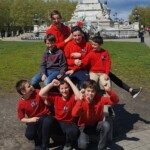 Équipe de jeunes en tenue rouge du club posant joyeusement en groupe devant un monument.