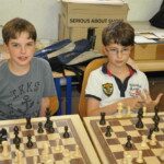 Deux jeunes joueurs souriants devant leurs échiquiers à la fin de la saison au club.