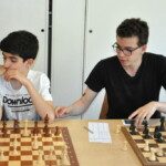 Un jeune joueur et son adversaire souriants devant l'échiquier lors d'une séance de fin de saison au club.