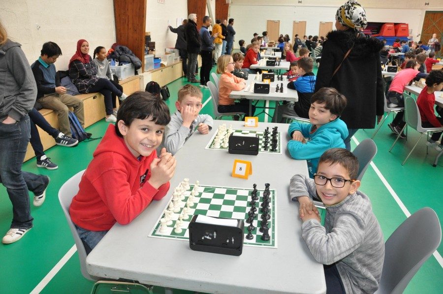 Quatre jeunes joueurs souriants autour de leurs échiquiers lors de l'étape de Nozay du Grand Prix.