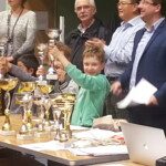 Un jeune joueur reçoit sa coupe devant une table couverte de trophées au Championnat Écoles et Collèges.