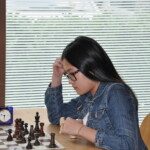 Une joueuse concentrée, la main sur le front, réfléchit devant son échiquier lors du Grand Prix Jeunes.