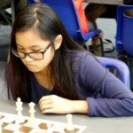 Une jeune joueuse à lunettes place ses pièces avant une ronde des championnats jeunes de l'Essonne.