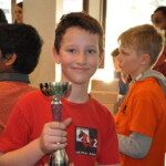 Jeune joueur du club en maillot rouge exhibant fièrement sa coupe au Grand Prix Jeunes de l'Essonne.