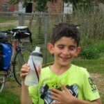 Un jeune cycliste souriant, gourde à la main, devant son vélo lors de la rando vélo vers l'Open de Dieppe.