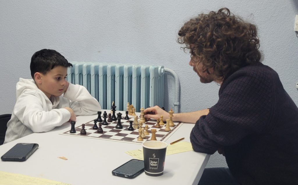 Un jeune joueur affronte un adulte sur un échiquier de club, championnats jeunes d'Île-de-France.