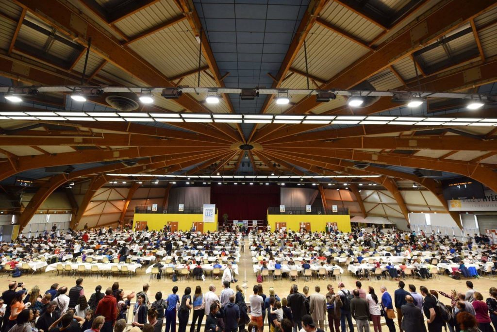 Vaste salle du Championnat de France jeunes à Hyères, avec des centaines de joueurs attablés.