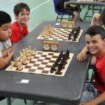 Trois jeunes joueurs souriants devant leurs échiquiers lors de la dernière étape à Juvisy.