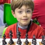 Jeune joueur souriant derrière son échiquier au Championnat de France jeunes 2014 à Montbéliard.