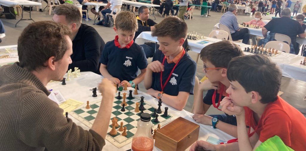 Un entraîneur analyse une partie sur l'échiquier avec de jeunes joueurs aux championnats de France.